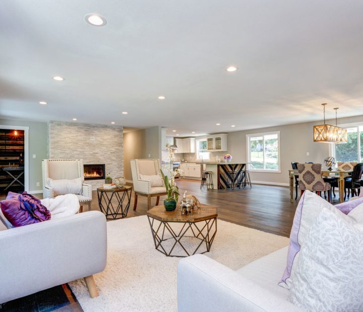A beautifully remodeled open-concept living area featuring a stone fireplace, modern furniture, hardwood flooring, recessed lighting, and a seamless transition to the kitchen and dining space.